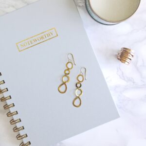 pair of gold-colored dangling hook earrings on top of spiral notebook